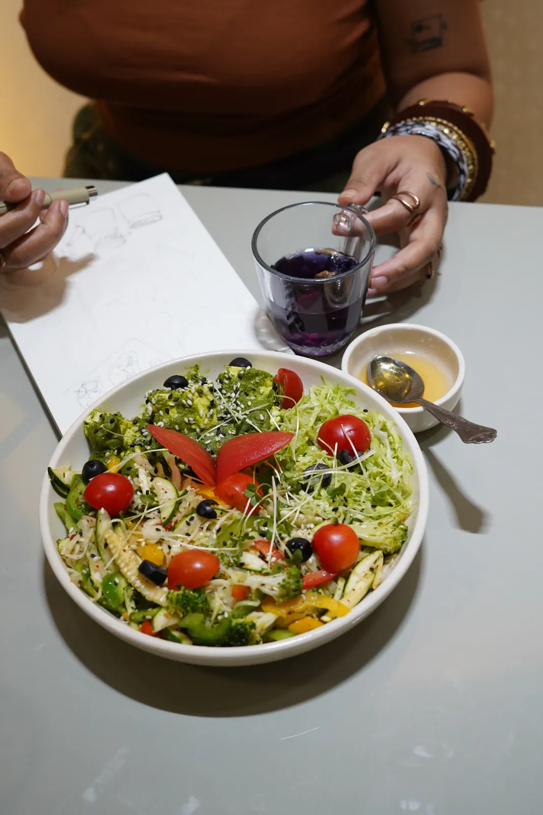 A large salad bowl with greens, cherry tomatoes and olives, served with dressing on the side at the Satvik Salaad café