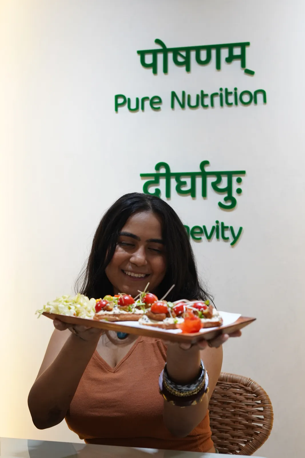 A guest holding a toast platter in front of the Satvik Salaad café wall reading Pure Nutrition and Longevity